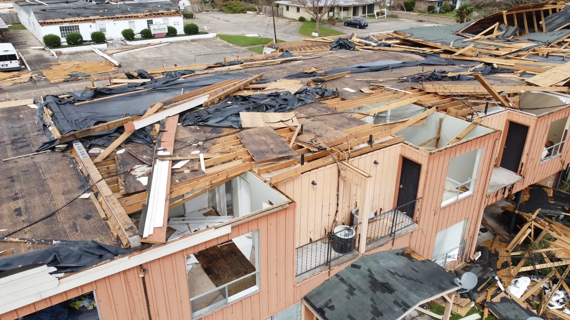An aerial view of a commercial building with its roof membrane and decking peeled back by storm damage.