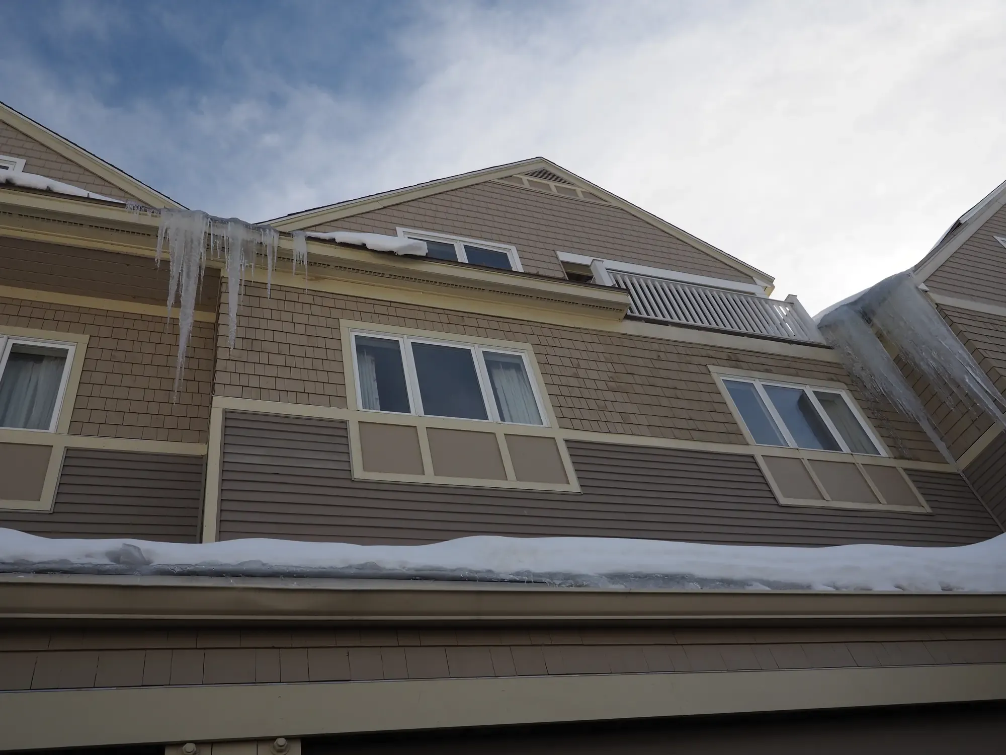 Ice built up along the eave of a New England home, with icicles hanging from the gutter line and snow on the roof below.