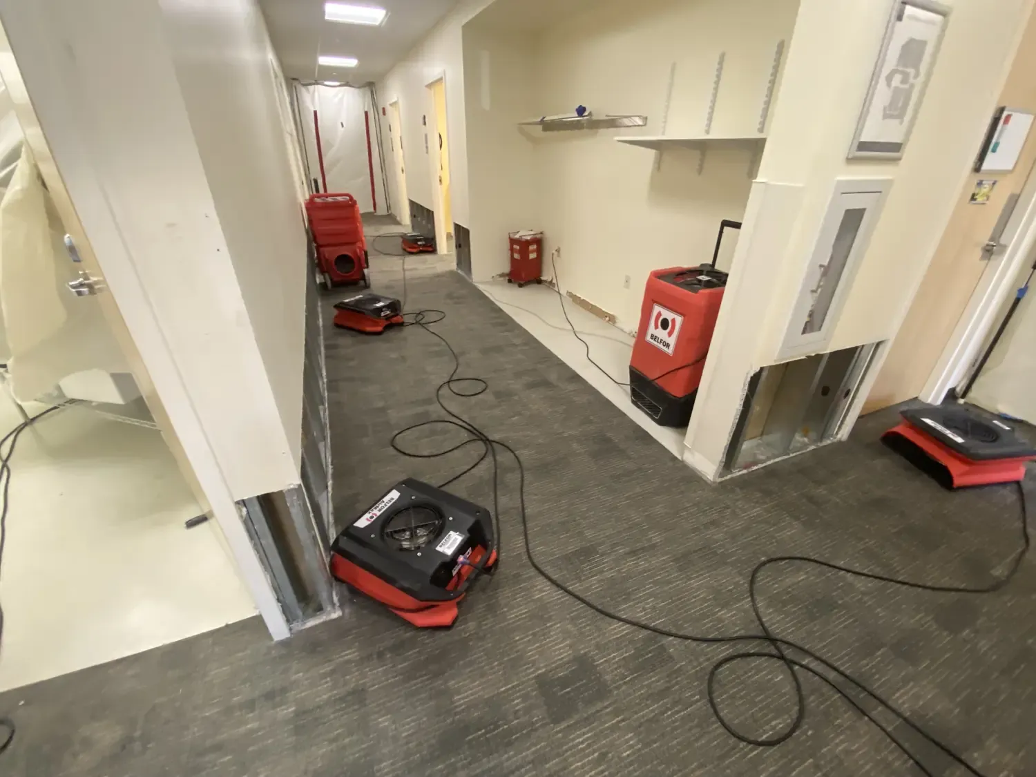 A commercial hallway under active mitigation, with air movers and a dehumidifier drying the floor.